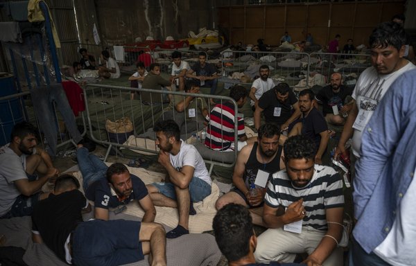 Survivors of a shipwreck sit inside a warehouse at the port in Kalamata, Greece, on June 15, after a boat carrying migrants sank in international waters in the Ionian Sea. [Angelos Tzortzinis/Pool/AFP]