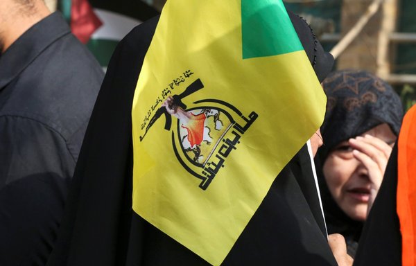 An Iraqi woman lifts a flag of the Iran-backed Kataib Hizbullah militia during a rally on Baghdad's Aba Nawas street on April 29, 2022. [Sabah Arar/AFP]
