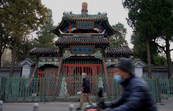 رجال يمشون بجوار مسجد نيوجي المغلق في بيجين في 3 نيسان/أبريل 2022. عمدت الصين إلى تدمير أي بناء في المساجد تتميز هندسته المعمارية بالطراز العربي والإسلامي كالمآذن والقبب، كجزء من خطة "الصيننة" التي تنفذها الحكومة. [نويل سيليس/وكالة الصحافة الفرنسية]