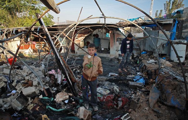 A Syrian boy holds a rose inside a charred tent following Syrian regime bombardment on a makeshift camp in the Idlib province village of al-Qah on November 21, 2019. [Aaref Watad/AFP]