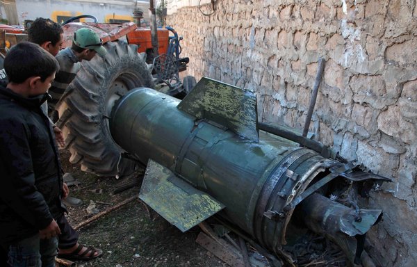 Syrians look at a fragment of a ground-to-ground missile fired by regime forces that hit a displacement camp in the Idlib village of al-Qah on November 21, 2019. [Aaref Watad/AFP]