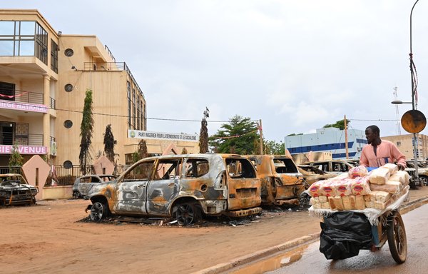 A street vendor pushes his cart past torched cars outside the headquarters of Nigerien president Mohamed Bazoum's Nigerien Party for Democracy and Socialism in Niamey on August 7, after a July coup that overthrew Bazoum. [AFP]